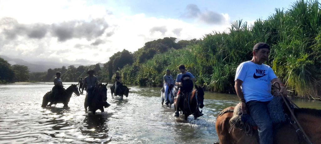 hombres en caballo pasando riocabalgata en playa los naranjos